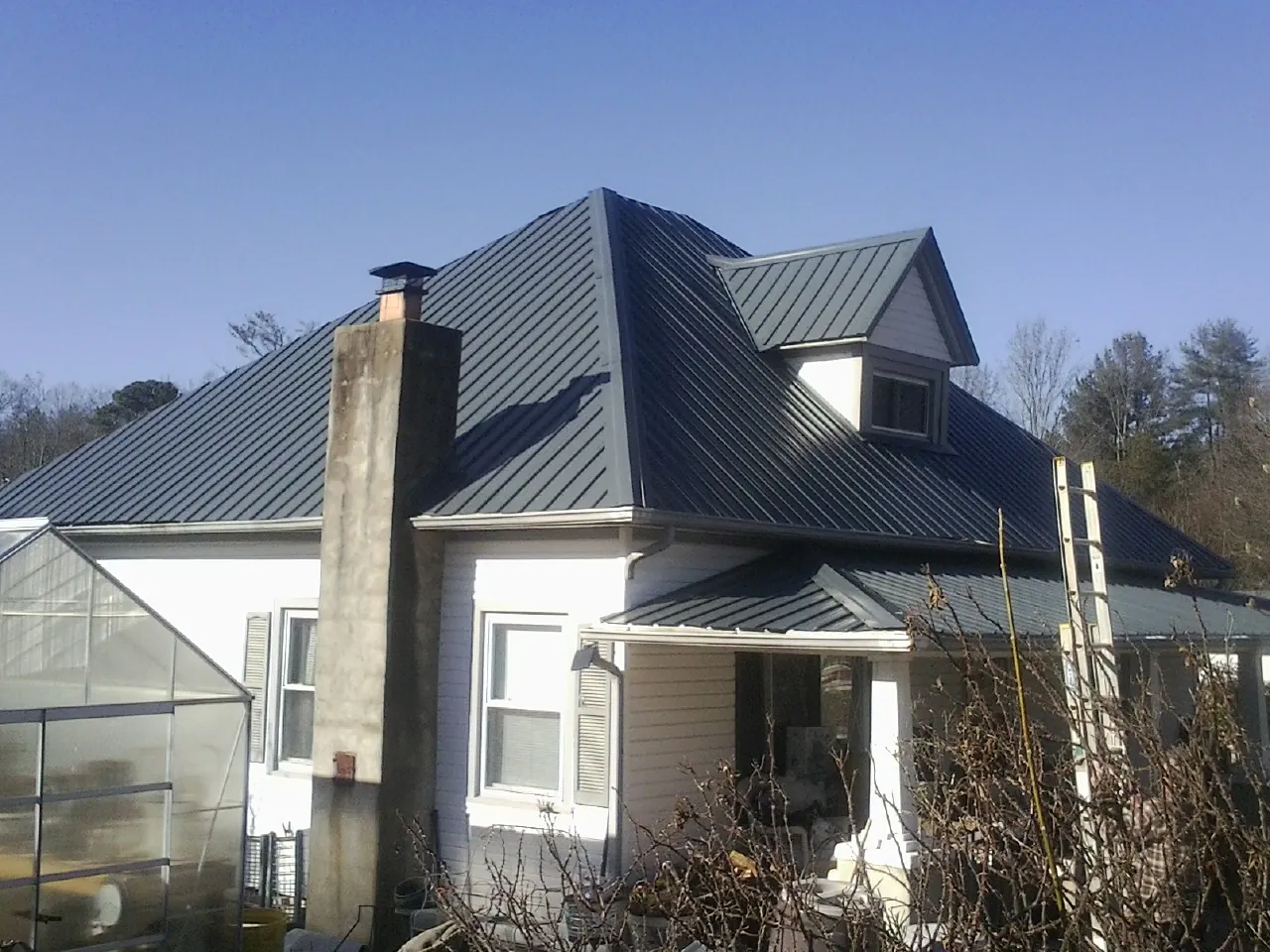 Dark blue standing seam metal roof on a white farmhouse with dormer — Slate & Tile Roof Repair by Roofing Brothers in White Earth