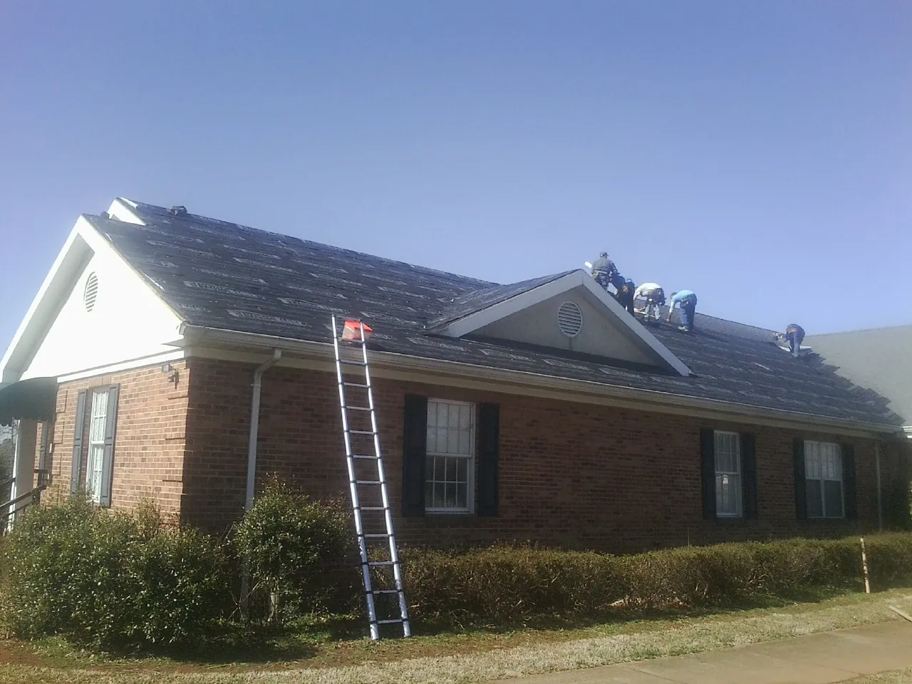 Crew tearing shingles off a brick ranch roof with a ladder set — Emergency Roof Repair work by our crew in White Earth
